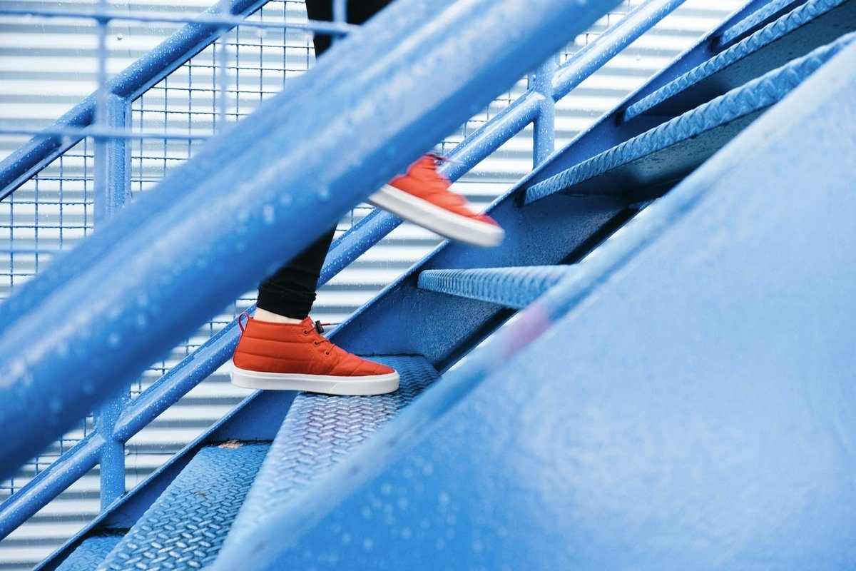 Pieds en baskets rouges qui montent un escalier métallique bleu